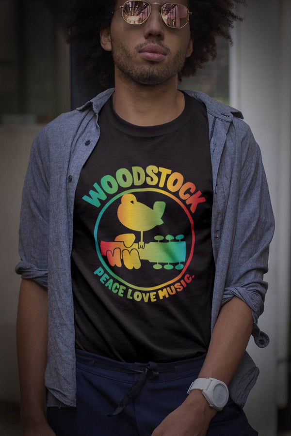 Woodstock rainbow graphic T-Shirt. Relive and celebrate the most iconic music festival in history. Woodstock surely was 3 days of peach and music.white graphic on black shirt dove settling on guitar neck with fingers over neck  I  Offbeet Shirts